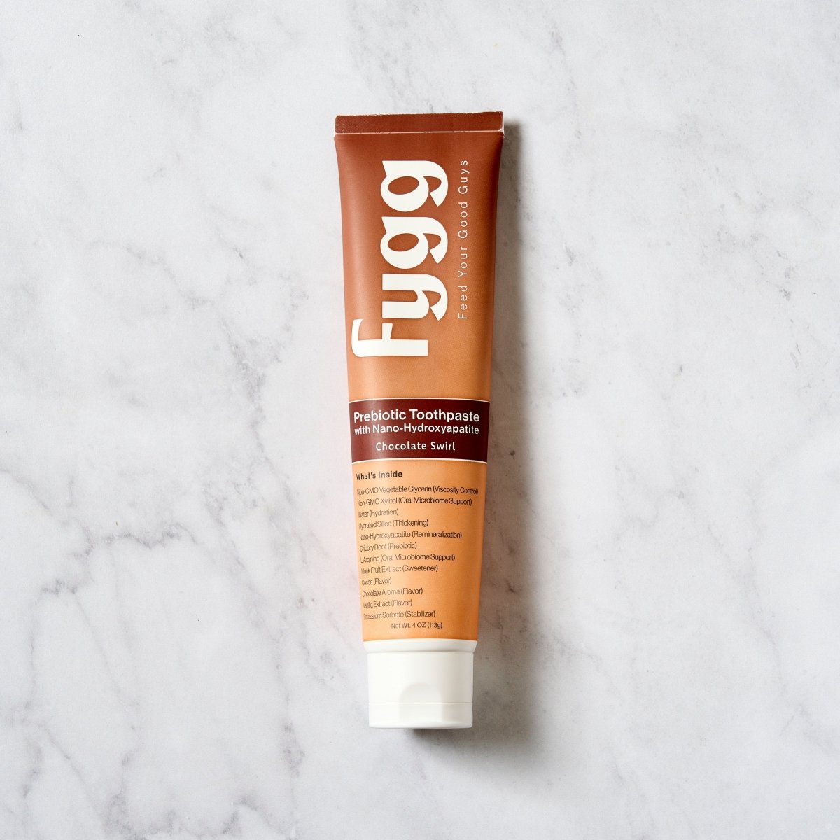 A squeeze tube of Fygg Probiotic Toothpaste in Chocolate Bean flavor, standing vertically on a white marble surface.