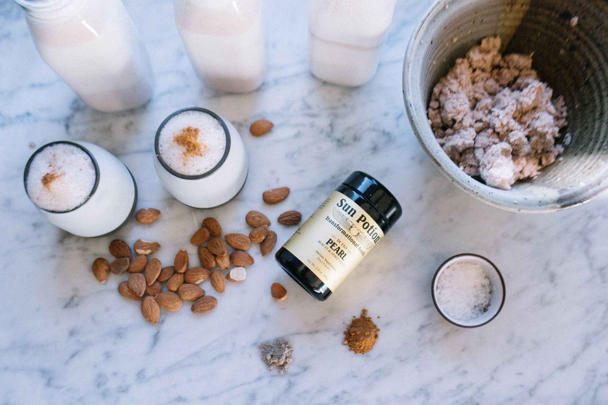 Sun Potion Pearl Powder jar lying on marble beside lattes, almonds and a bowl of granola