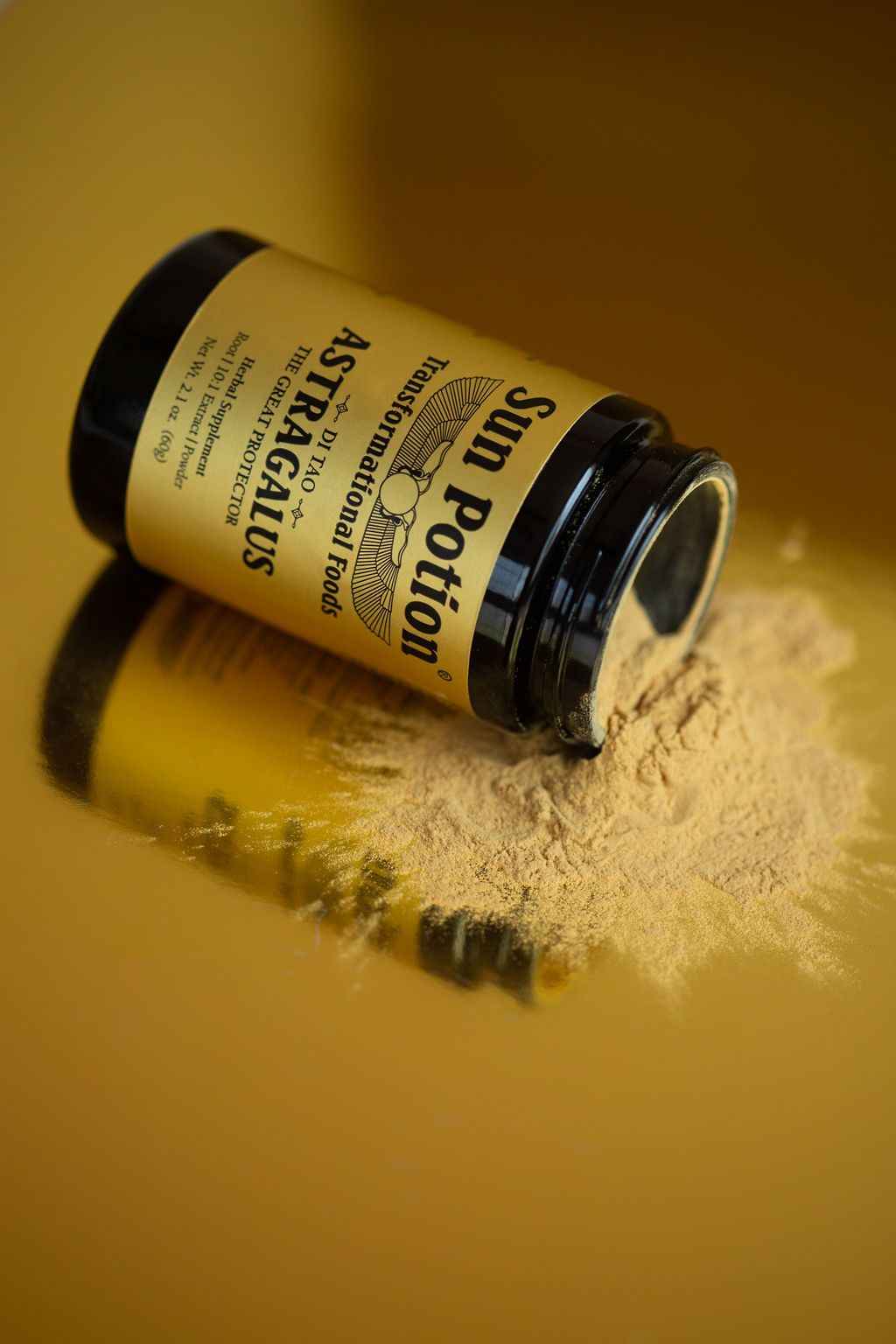 Sun Potion Astragalus jar lying on its side on a gold surface with spilled powder