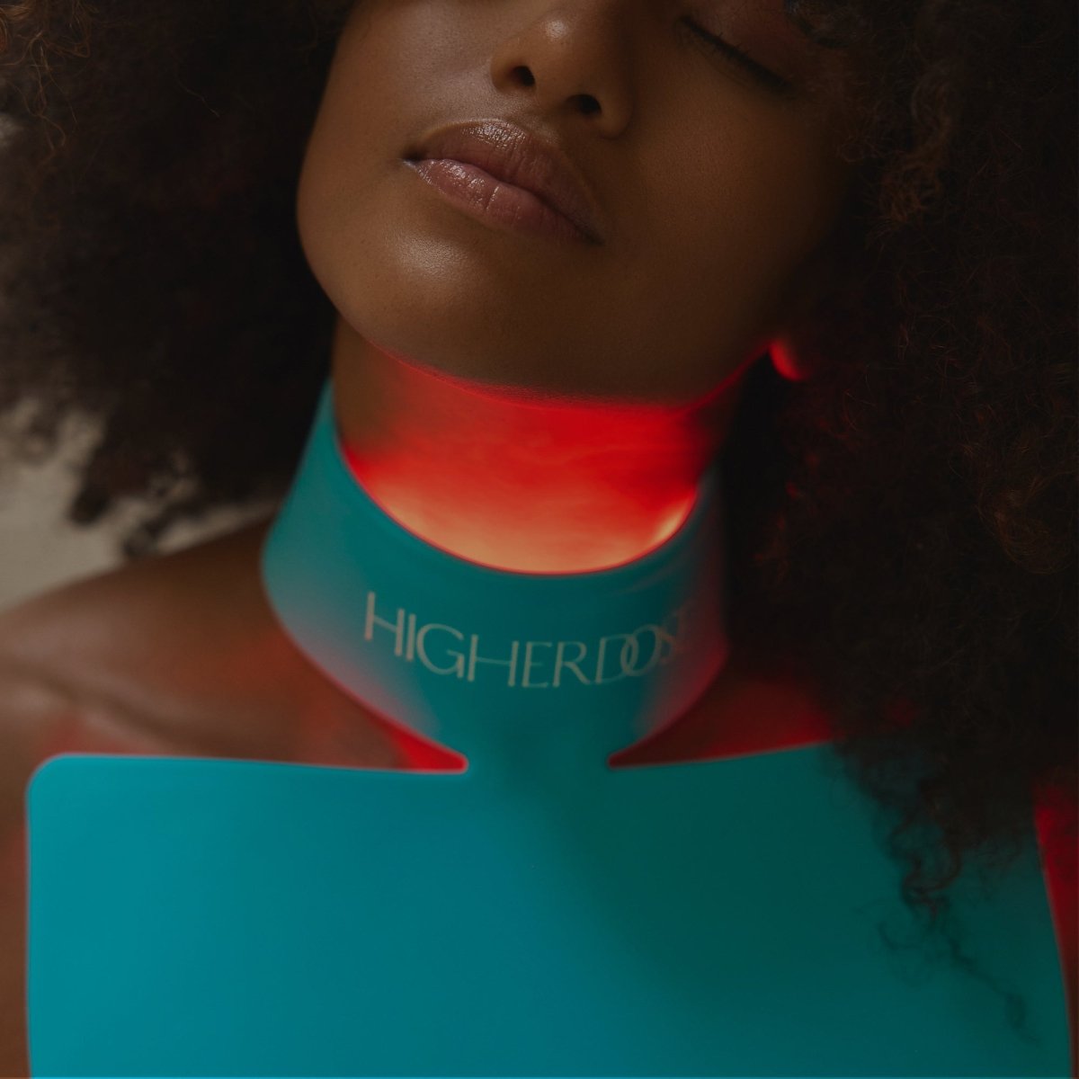 Close-up of a neck glowing red under the HigherDOSE Red Light Neck Enhancer, alternate crop