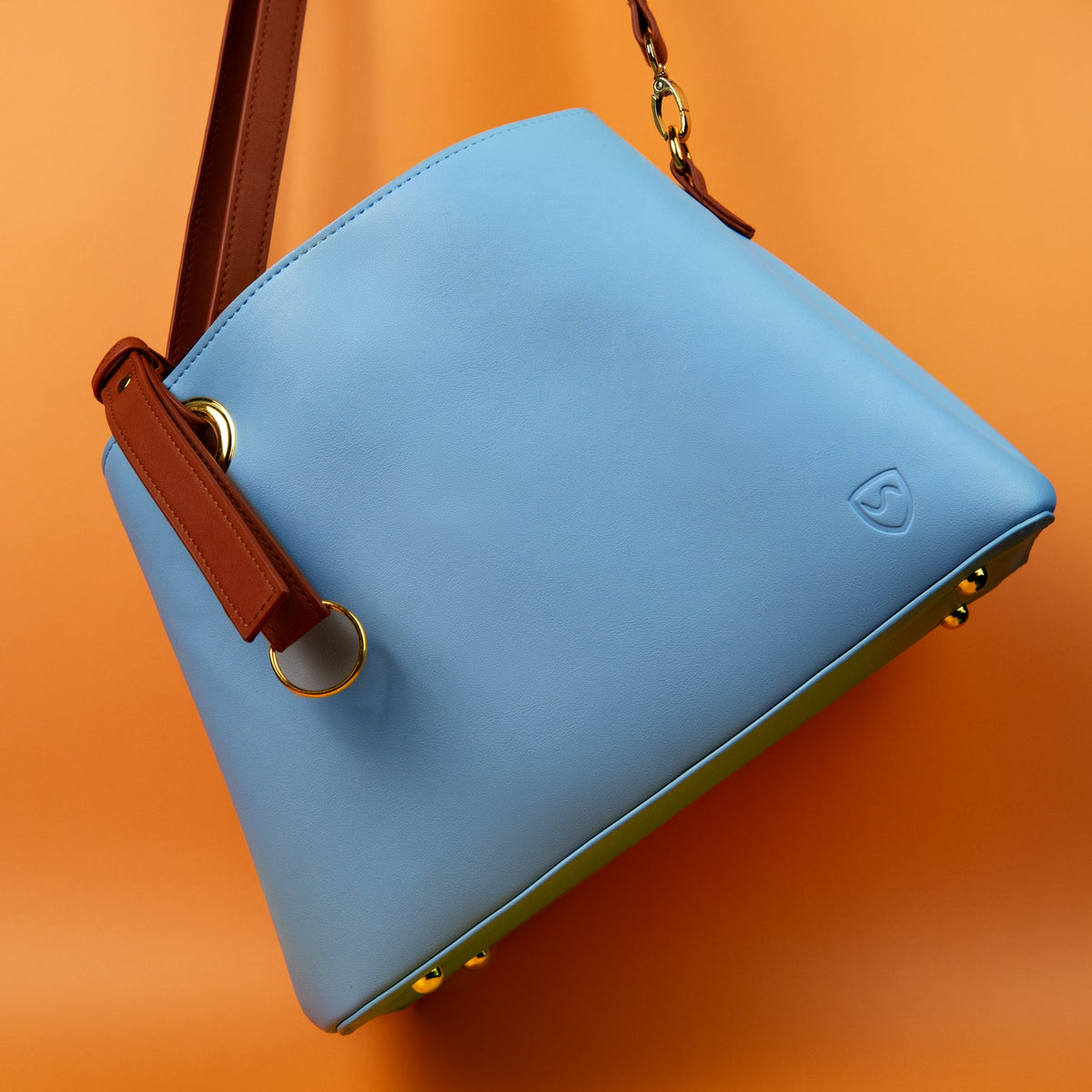 Shield Your Body blue Purse tilted on an orange background with brown strap loops