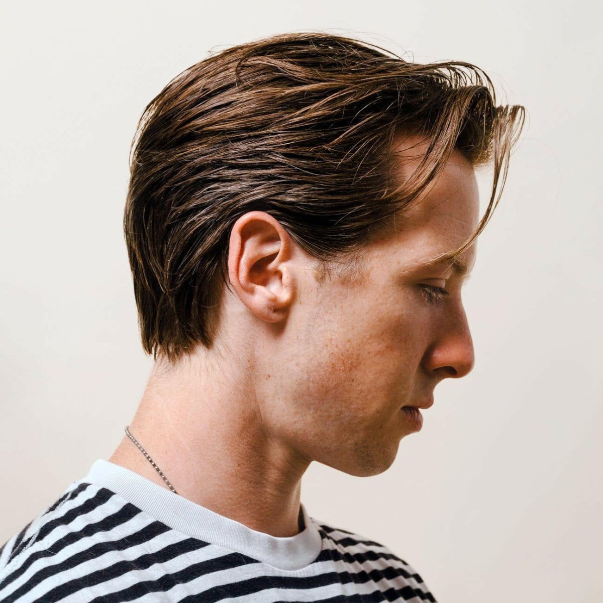 Side profile of a man with a swept hairstyle and striped shirt, styled with Firsthand Supply Texturizing Paste