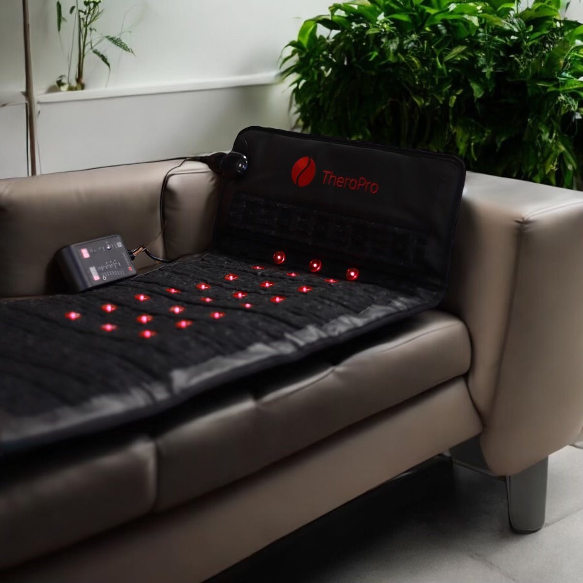 Therasage TheraPro pad with red lights glowing on a sofa beside a plant