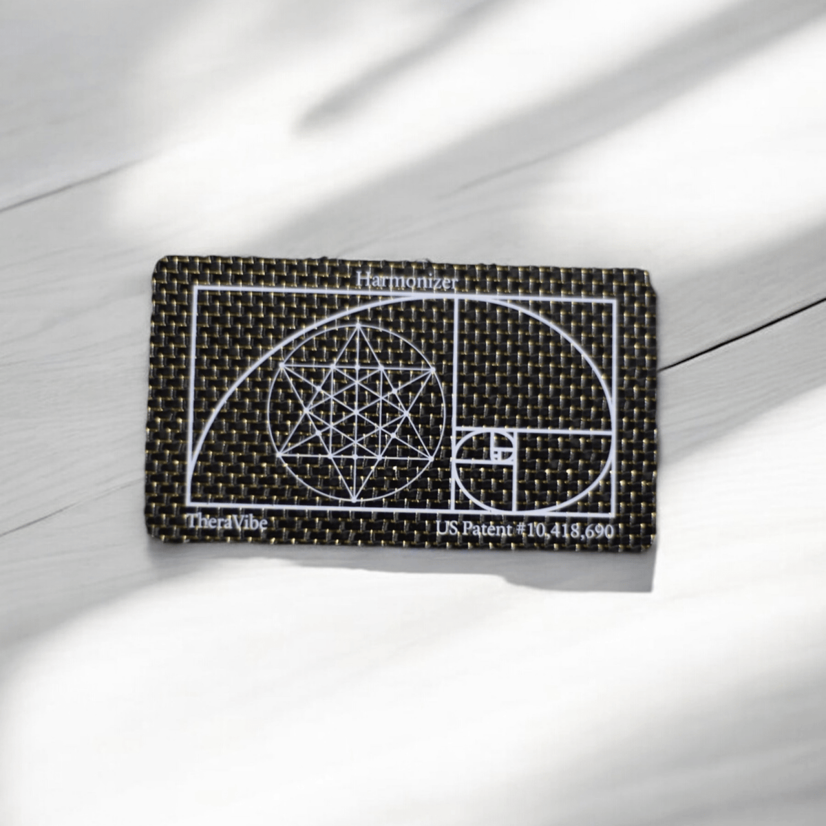 Therasage TheraVibe Quantum Card with golden ratio spiral on a white wood surface
