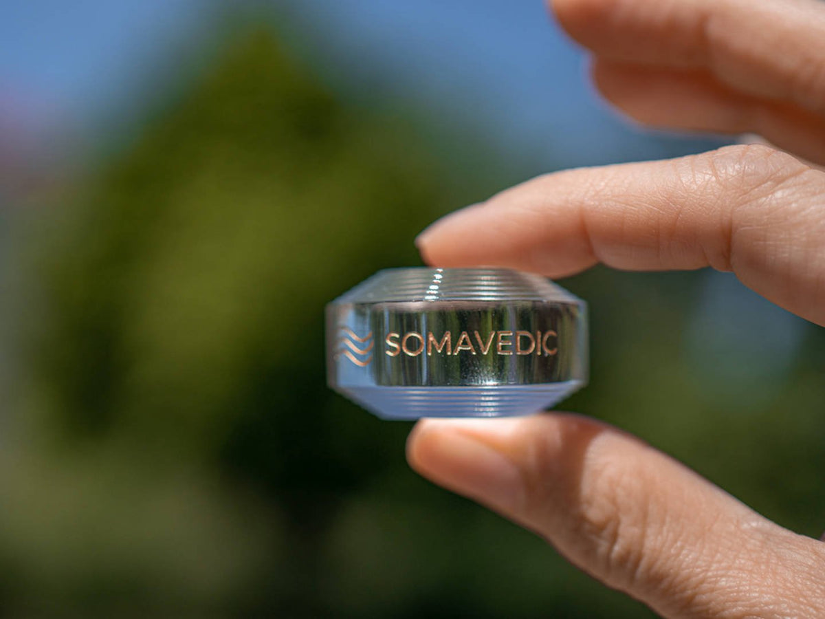 Fingers holding the Somavedic Tiny clear against a green blurred background
