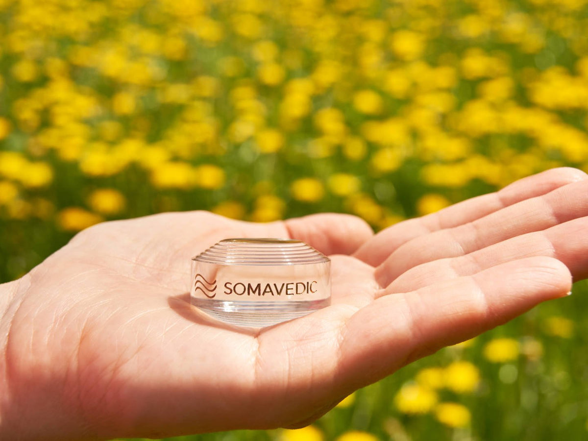 Palm holding the Somavedic Tiny clear in a field of yellow flowers
