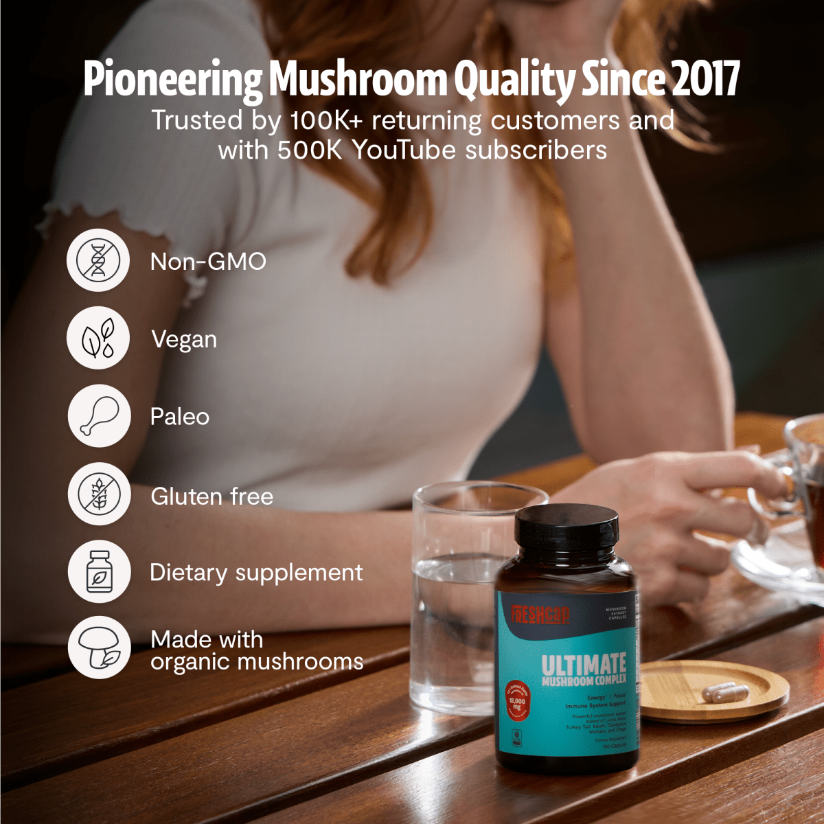 Woman at a table with a bottle: FreshCap Mushrooms Mushroom Complex Capsules, pioneering quality since 2017, non-GMO, vegan