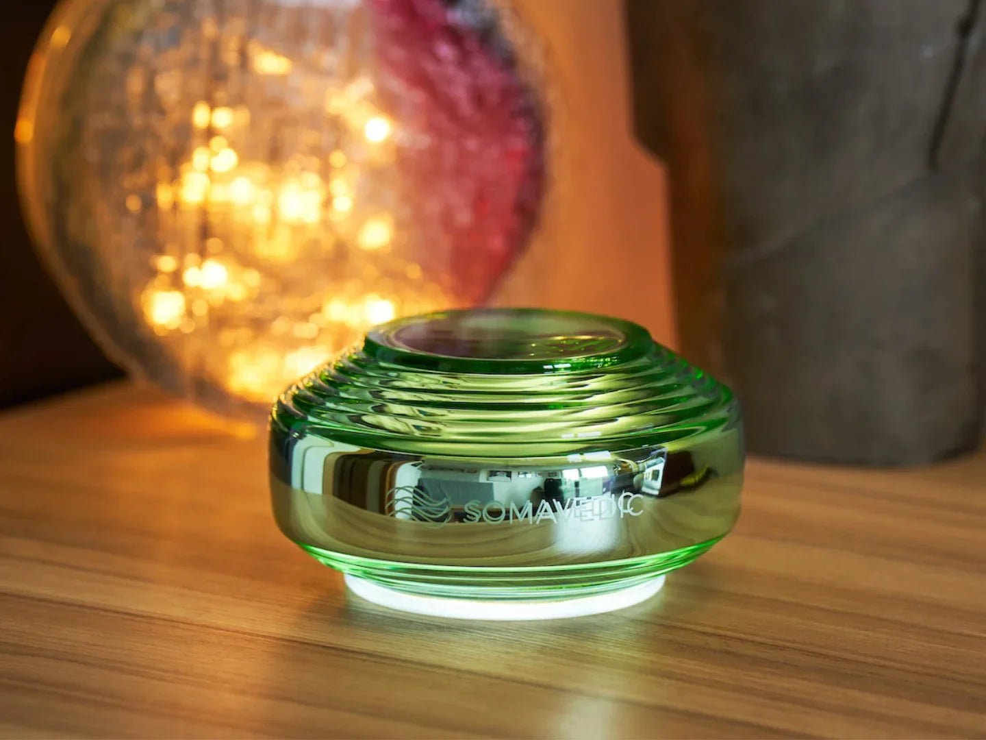 Green glass container with 'SOMA' branding on a wooden surface with blurred lights in the background